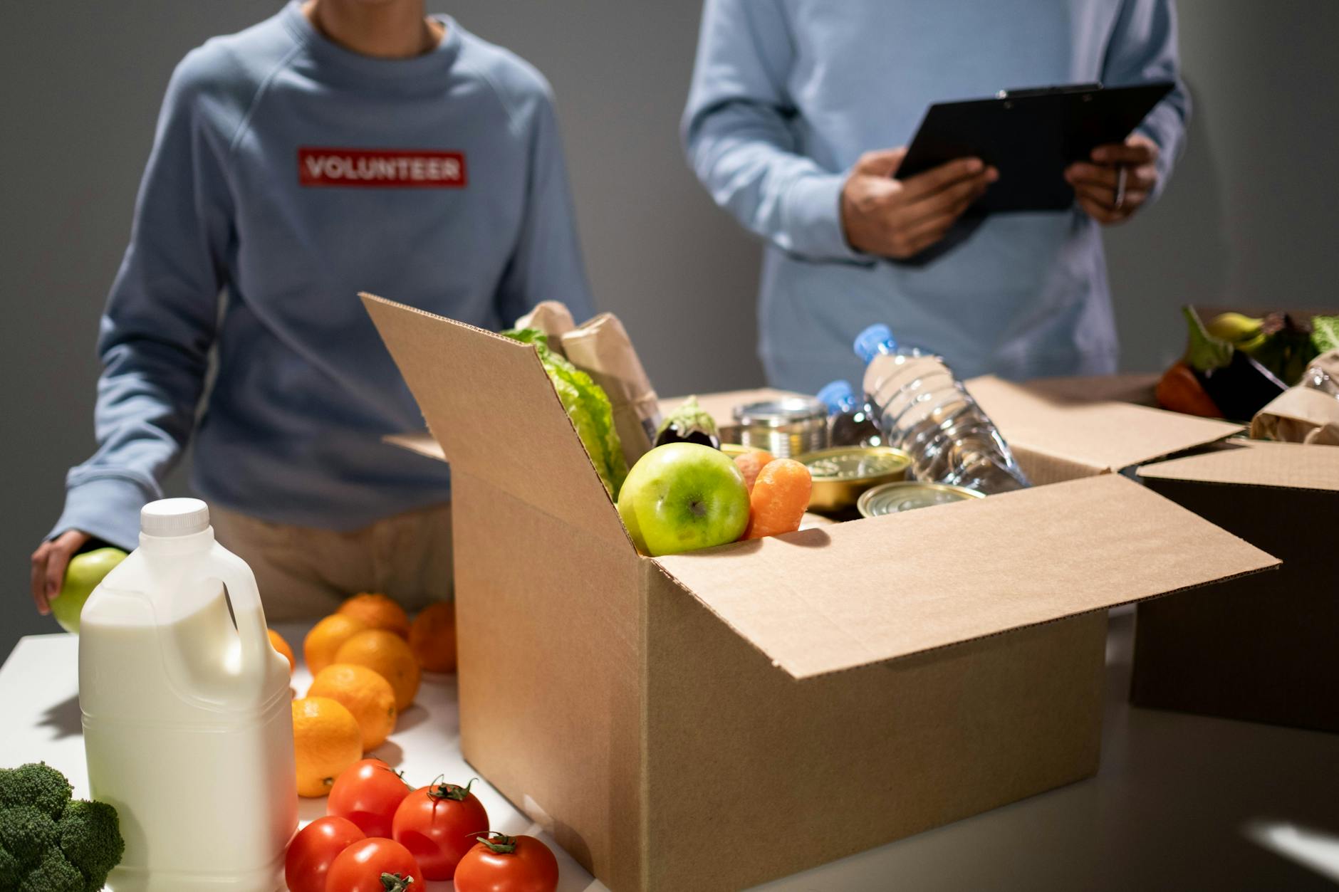 Home People packing a cardboard box with essentials like fruits, vegetables, and bottled water for charity.